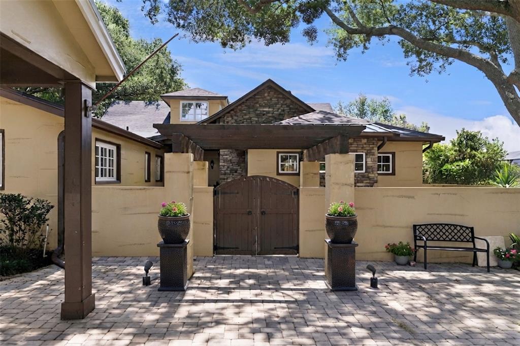A paved courtyard features a wooden gate, a pergola, and two large potted plants — 1629 HEMPEL AVENUE, WINDERMERE, FL