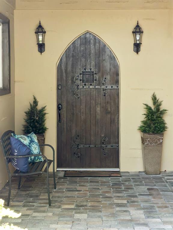A dark wood arched door with decorative iron hinges sits between two wall-mounted lanterns — 1629 HEMPEL AVENUE, WINDERMERE, FL