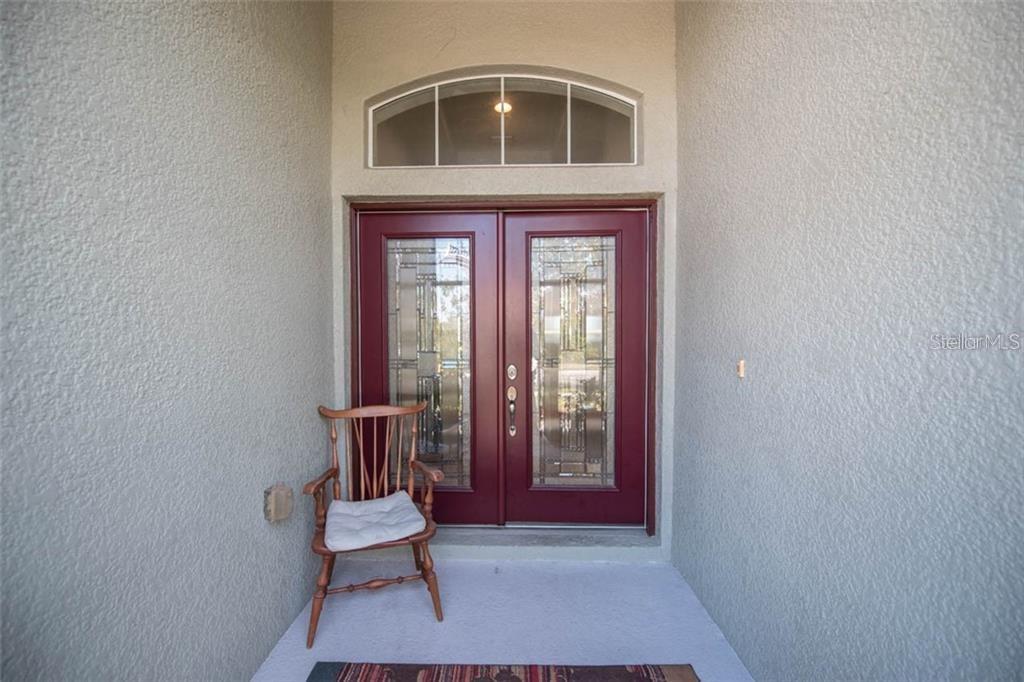 A wooden chair sits on a concrete porch in front of double red glass-paneled doors — 1742 MIRA LAGO CIRCLE, RUSKIN, FL