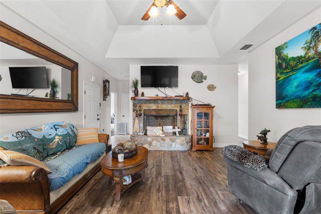 A living room features a stone fireplace, wood-look flooring, a vaulted ceiling, and coastal decor — 4190 NW 153RD COURT, CHIEFLAND, FL