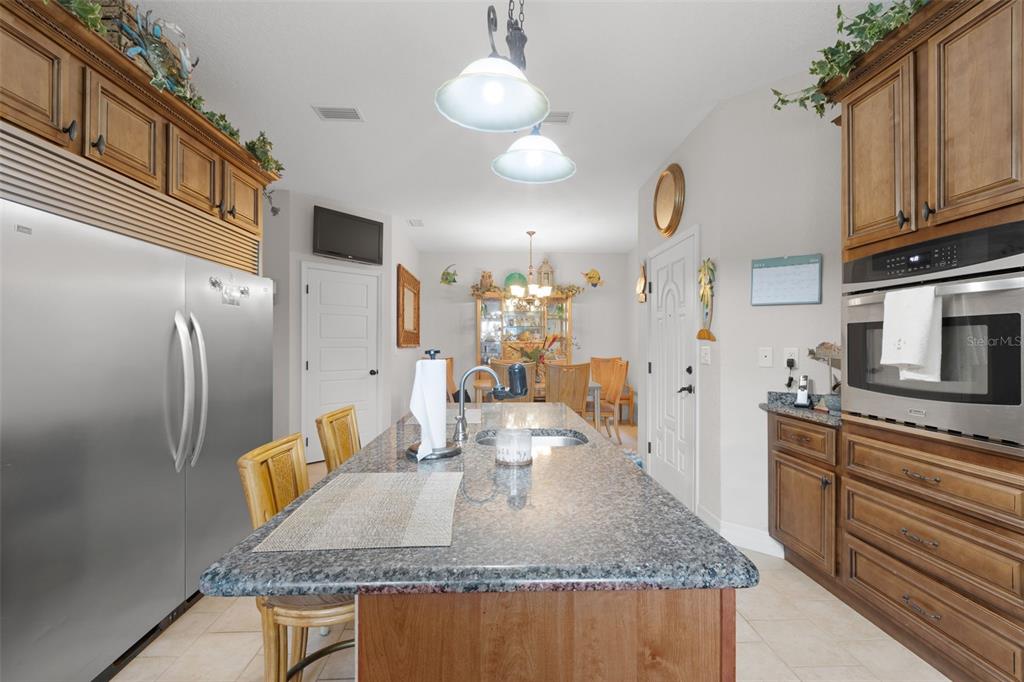 A kitchen features a granite-topped island, stainless steel appliances, and wooden cabinetry — 4190 NW 153RD COURT, CHIEFLAND, FL