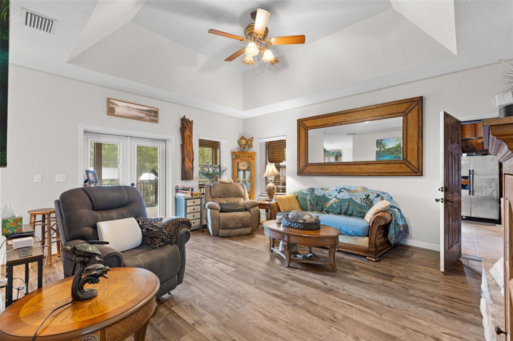 A living room with wood-look flooring, a vaulted ceiling, a ceiling fan, and a large mirror — 4190 NW 153RD COURT, CHIEFLAND, FL