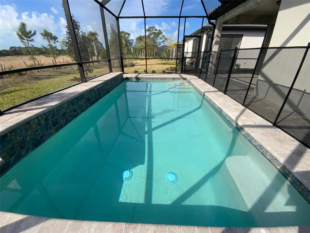 A rectangular swimming pool is enclosed within a screened lanai overlooking a grassy field — 6319 CRESTED EAGLE LANE, NOKOMIS, FL