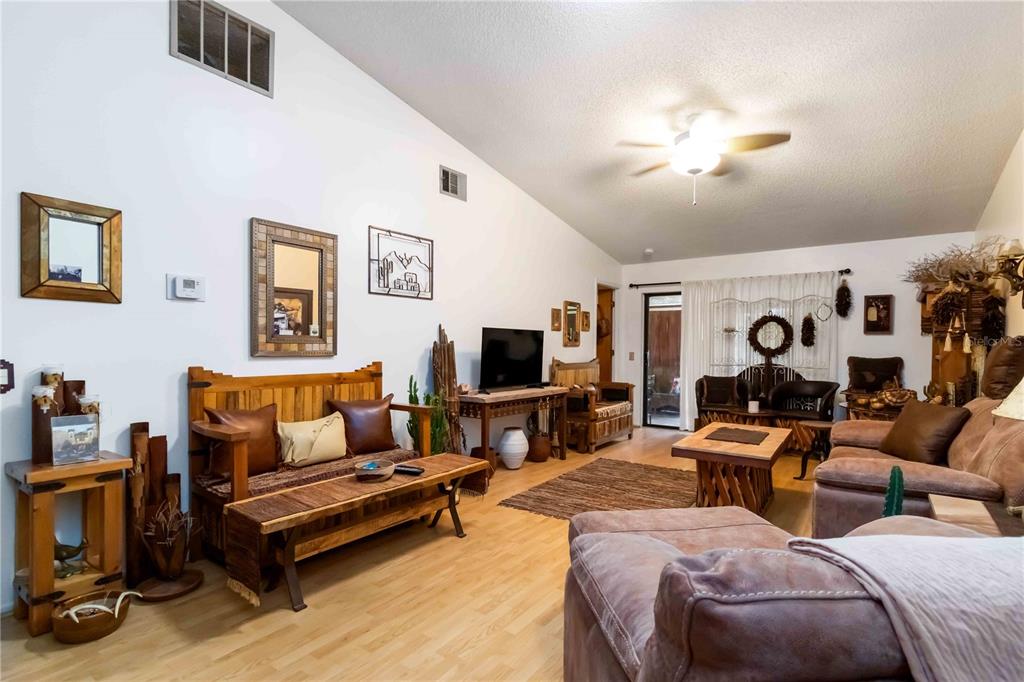 A living room features light wood flooring, a brown sofa, and a vaulted ceiling — 6521 HERITAGE LANE UNIT 2621, BRADENTON, FL