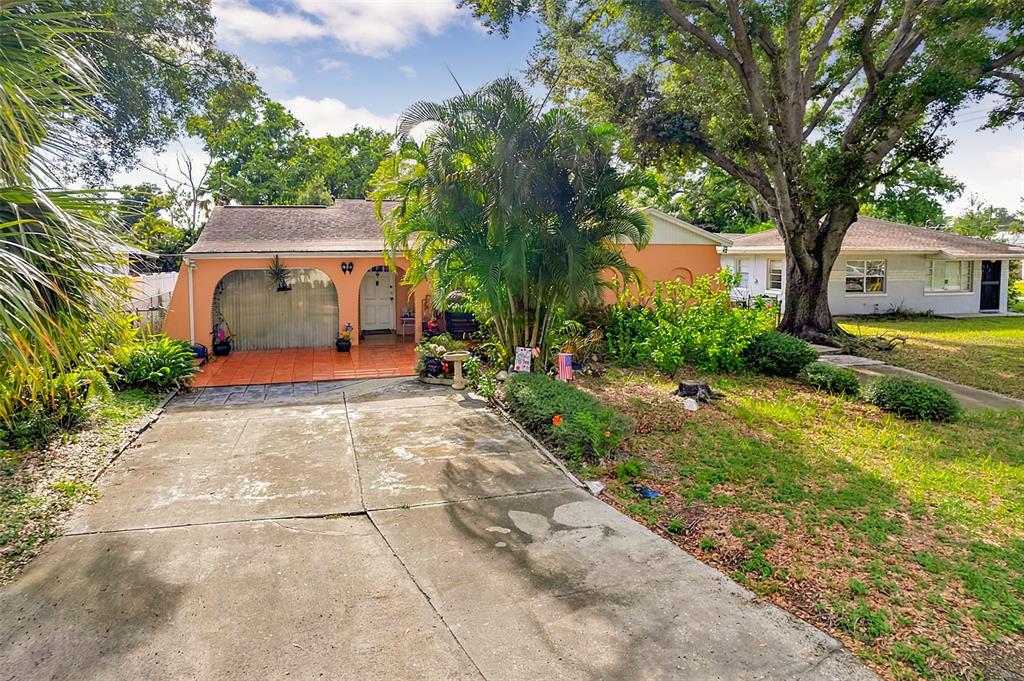 A single-story peach-colored house with a concrete driveway, a tiled porch, and large palm trees — 612 N WOODLYNNE AVENUE, TAMPA, FL