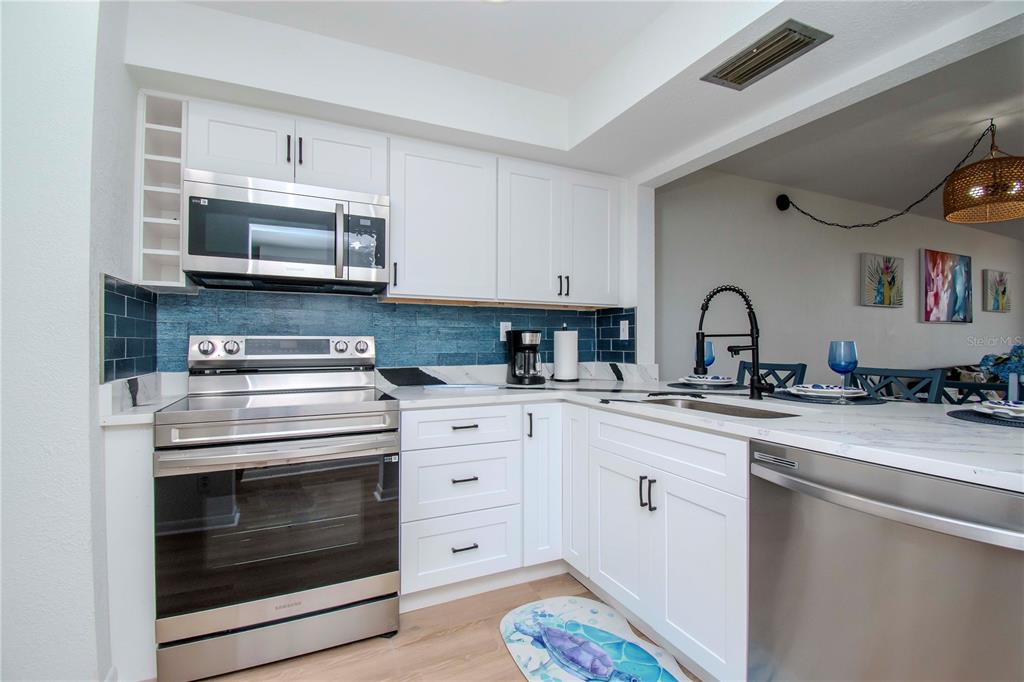 A kitchen features white cabinets, stainless steel appliances, and a blue subway tile backsplash — 6361 BAHIA DEL MAR BOULEVARD UNIT 605, ST PETERSBURG, FL