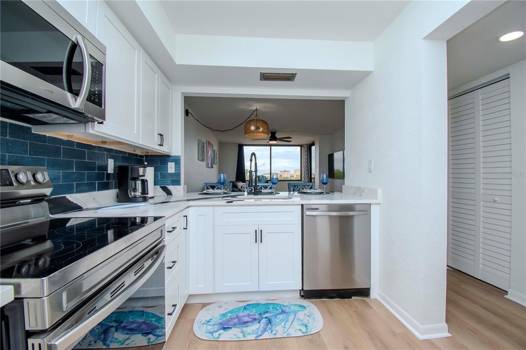 A kitchen with white cabinets, stainless steel appliances, and a blue tile backsplash faces a dining area — 6361 BAHIA DEL MAR BOULEVARD UNIT 605, ST PETERSBURG, FL