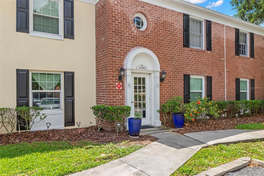 A gated entrance with a black metal fence and traffic bollards leads into a residential complex — 13762 ORANGE SUNSET DRIVE UNIT 102, TAMPA, FL
