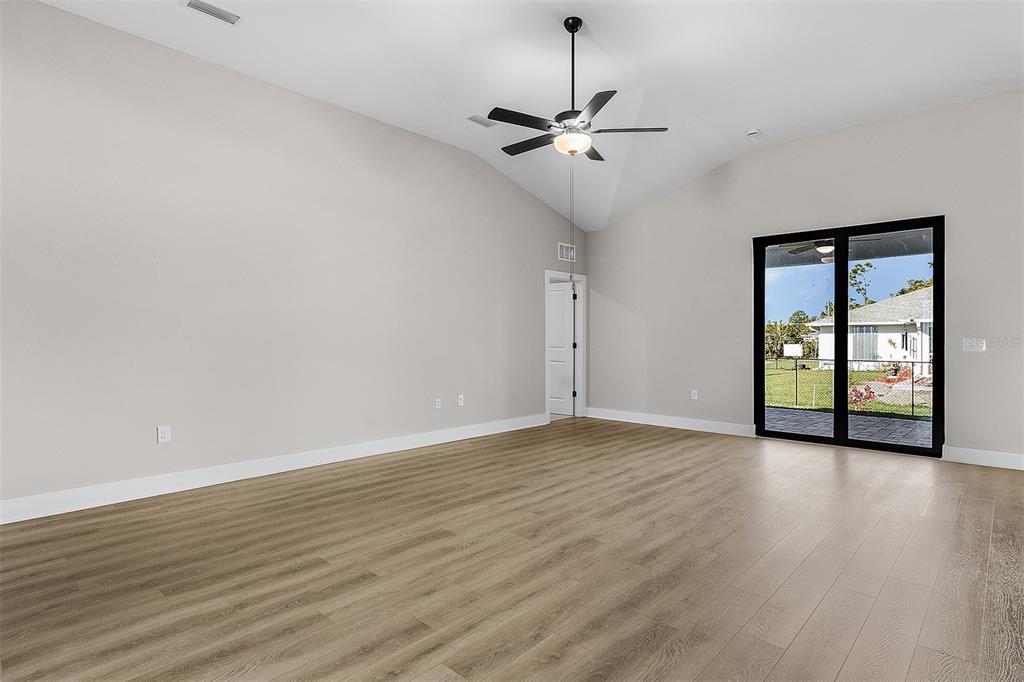A spacious room with light gray walls, wood-look flooring, a vaulted ceiling, and sliding doors — 13432 LAKE GALLAGHER DRIVE, DOVER, FL