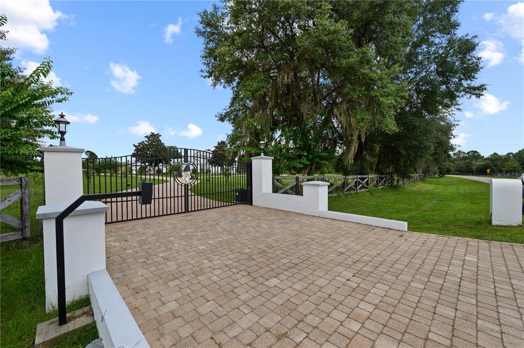 A paved driveway leads to a gated entrance with white pillars and a wooden fence — 1515 SW 112TH STREET, GAINESVILLE, FL