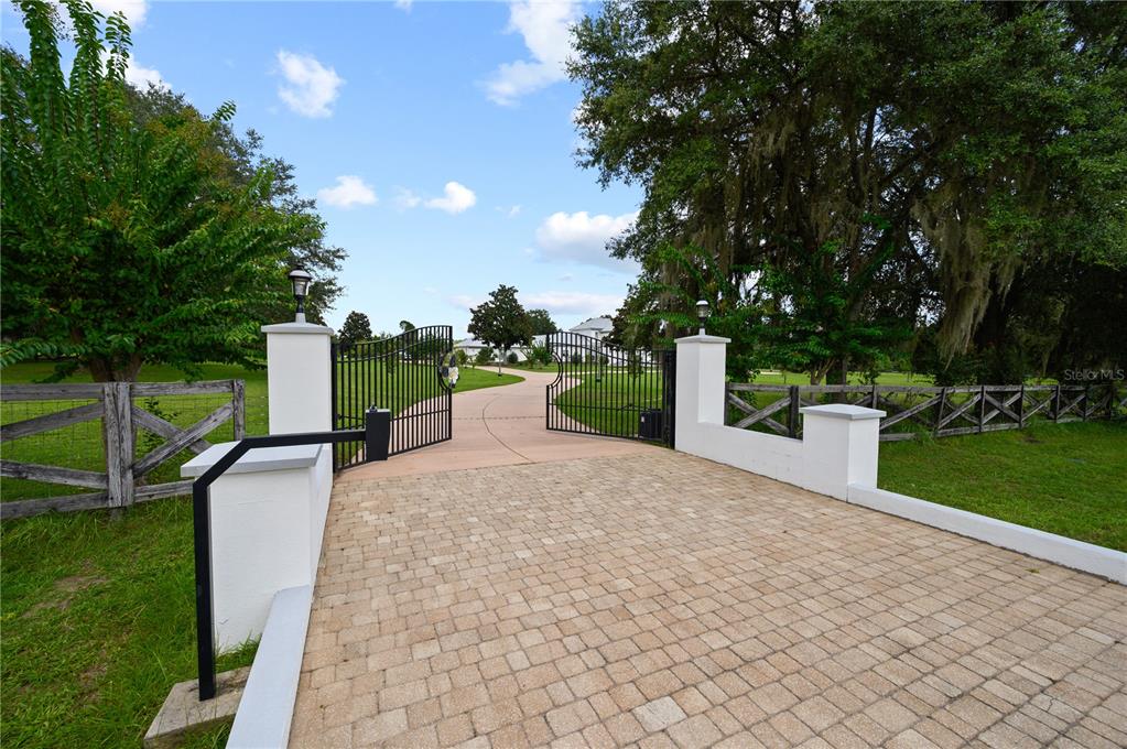 A paved driveway leads through an open wrought iron gate flanked by white masonry pillars — 1515 SW 112TH STREET, GAINESVILLE, FL