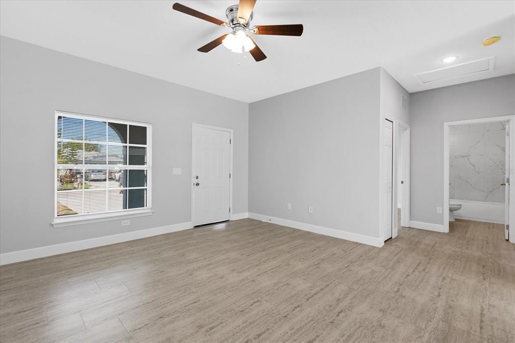 An empty room with light gray walls, wood-look tile flooring, a ceiling fan, and an attached bathroom — 16 TROUT WAY UNIT A & B, POINCIANA, FL