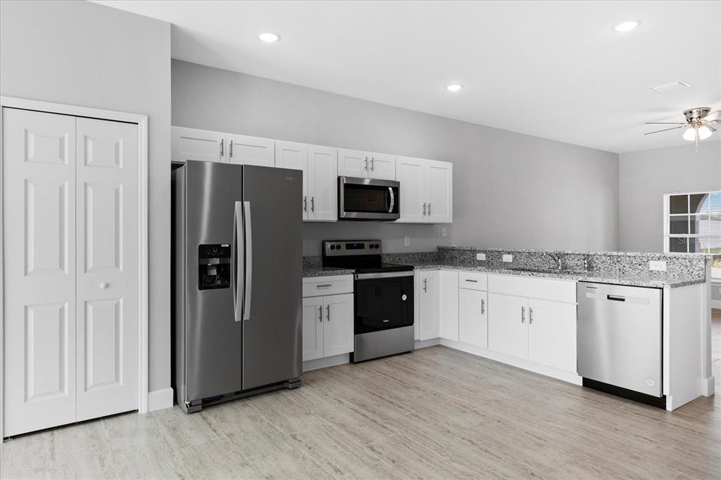 A kitchen with white cabinets, granite countertops, stainless steel appliances, and light wood-look flooring — 16 TROUT WAY UNIT A & B, POINCIANA, FL