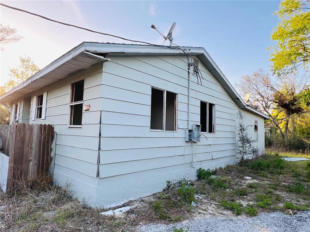 The exterior of a light-colored, single-story house with missing window panes and exposed electrical wiring — 20715 SE 141ST PLACE, UMATILLA, FL