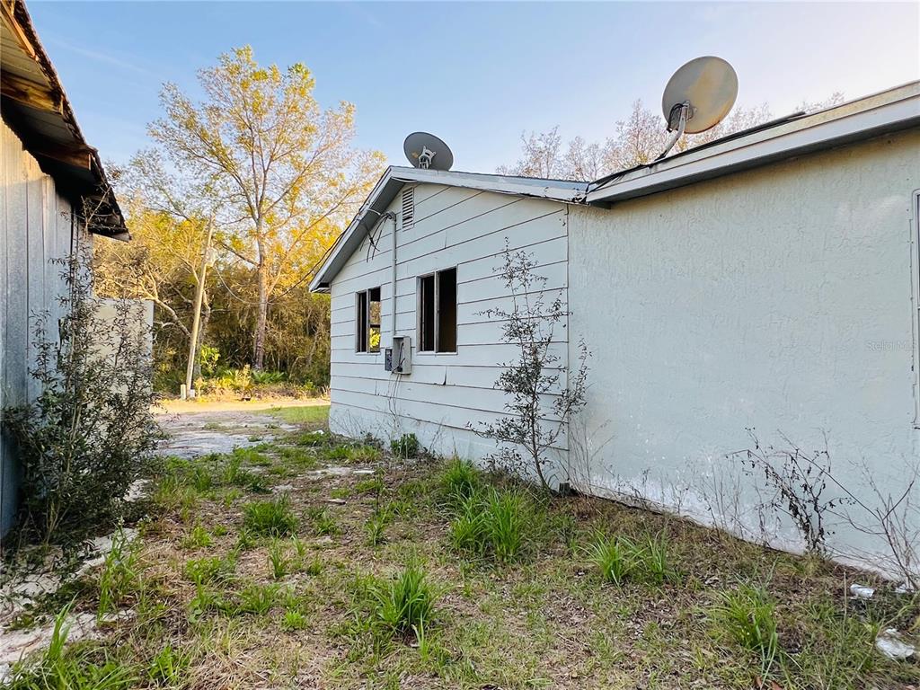 The exterior side of a light-colored house features two satellite dishes and two window openings — 20715 SE 141ST PLACE, UMATILLA, FL