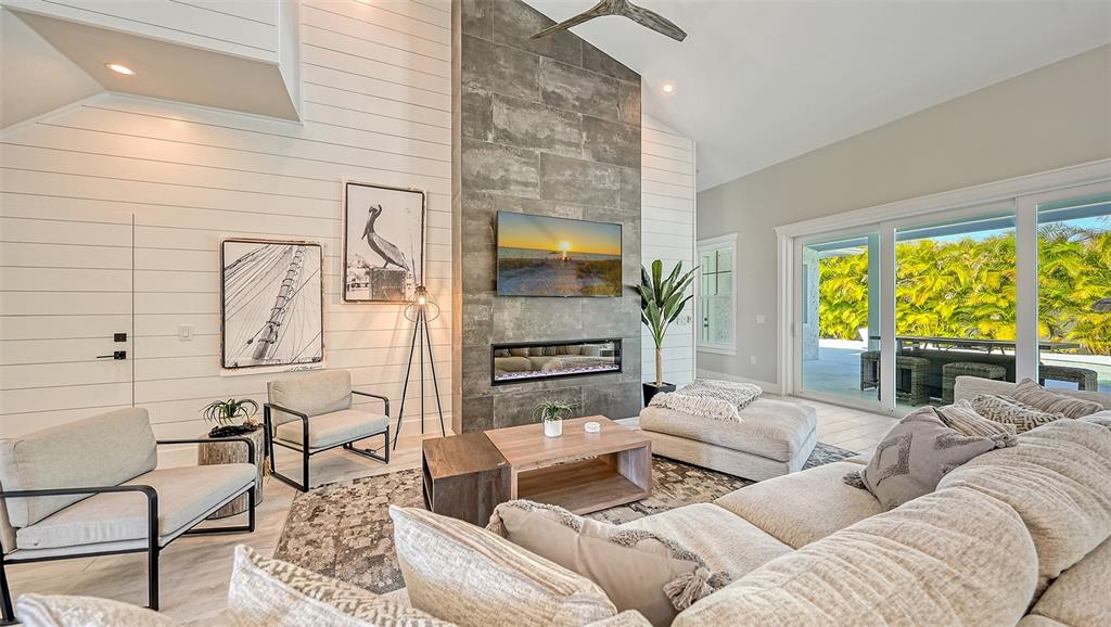 A modern living room features a stone fireplace, shiplap walls, and large sliding glass doors — 8006 20TH PLACE W, BRADENTON, FL