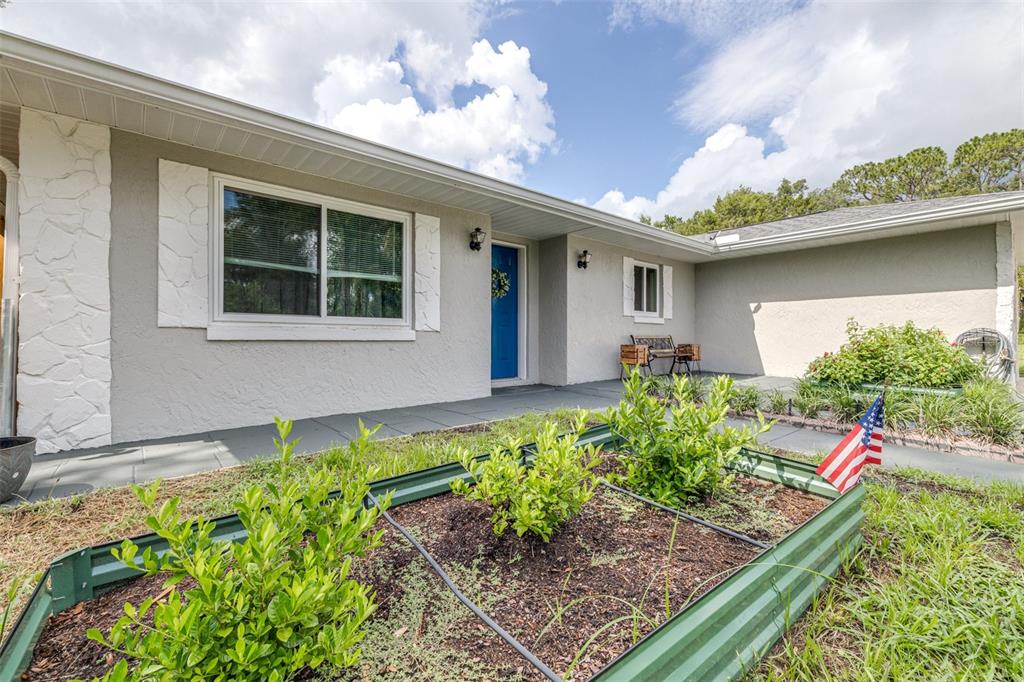 A single-story house exterior features a blue front door, gray stucco walls, and raised garden beds — 6330 E VALE STREET, INVERNESS, FL