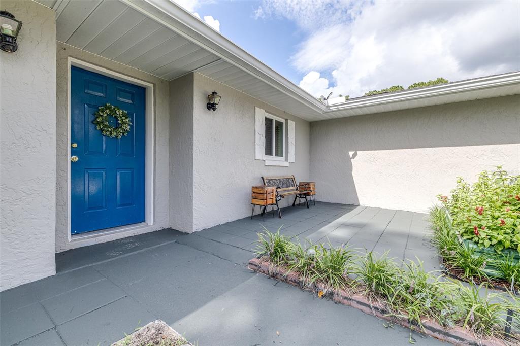 A blue front door opens onto a gray patio with a bench and garden bed — 6330 E VALE STREET, INVERNESS, FL