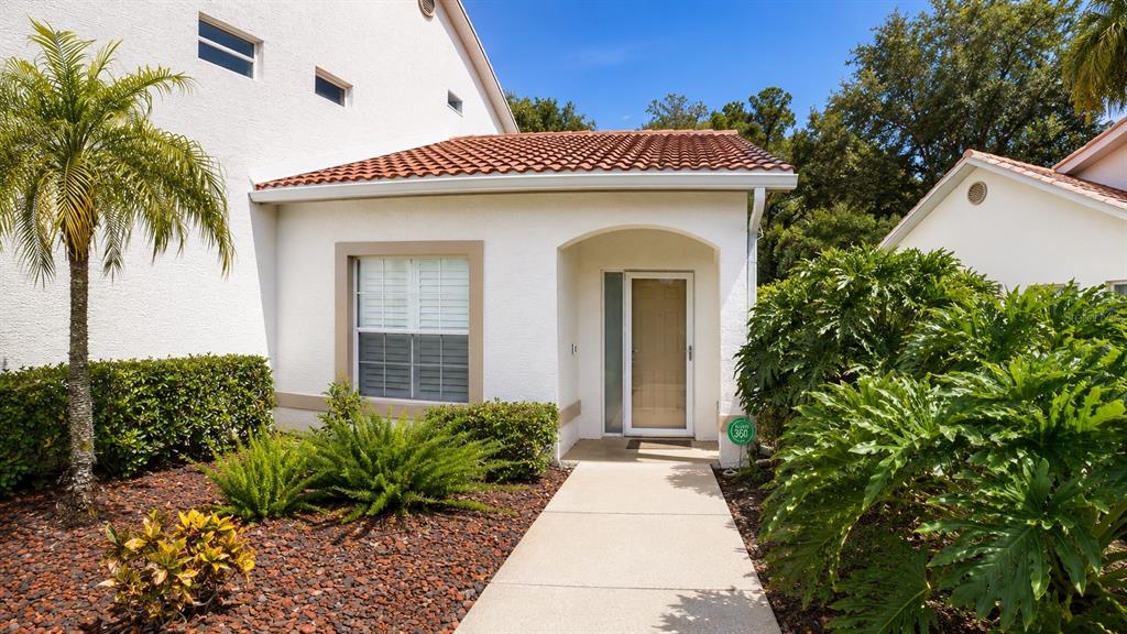 The exterior of a white house features a tiled roof, a front walkway, and landscaping — 5429 STONEYBROOK LANE UNIT 102, BRADENTON, FL