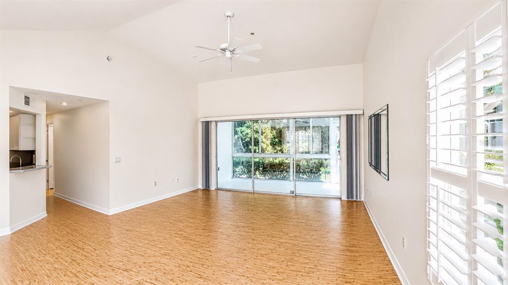 An empty living room features light wood flooring, a ceiling fan, and large sliding glass doors — 5429 STONEYBROOK LANE UNIT 102, BRADENTON, FL