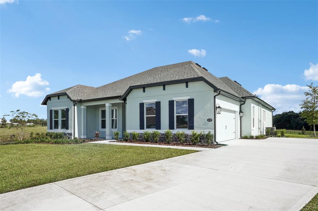 A single-story house with white stucco, blue shutters, and a stone base sits on grass — 36798 SUNDOWNER TRAIL, FRUITLAND PARK, FL