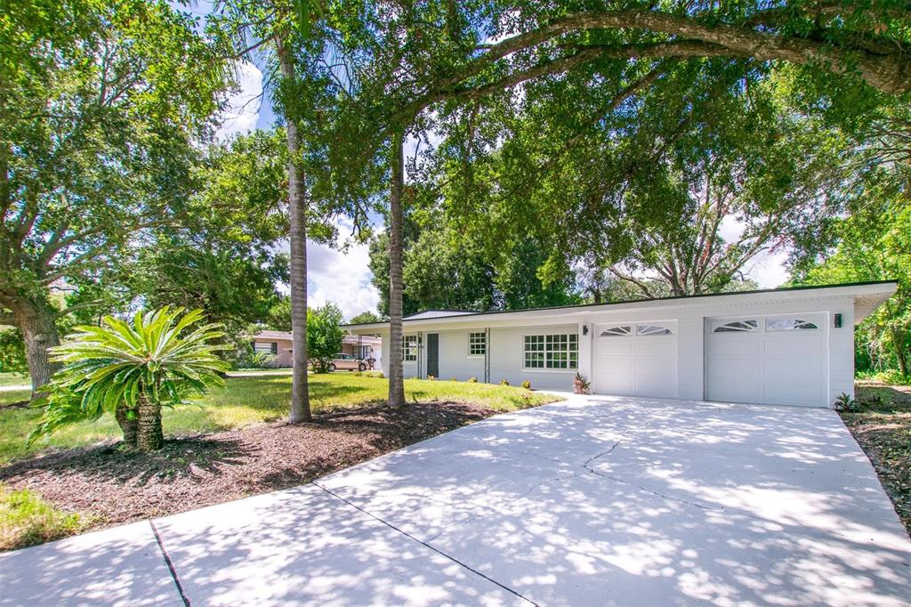 A white single-story house with a two-car garage and a concrete driveway under large trees — 1008 BERWYN ROAD, ORLANDO, FL