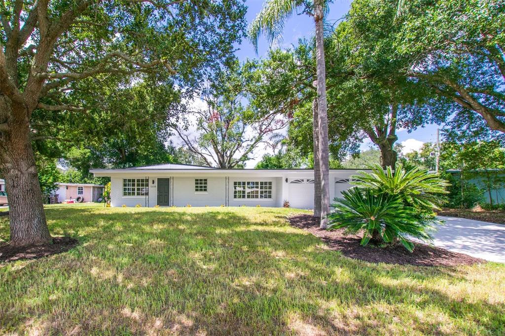 A single-story white house with a dark front door, garage, and mature trees in front — 1008 BERWYN ROAD, ORLANDO, FL