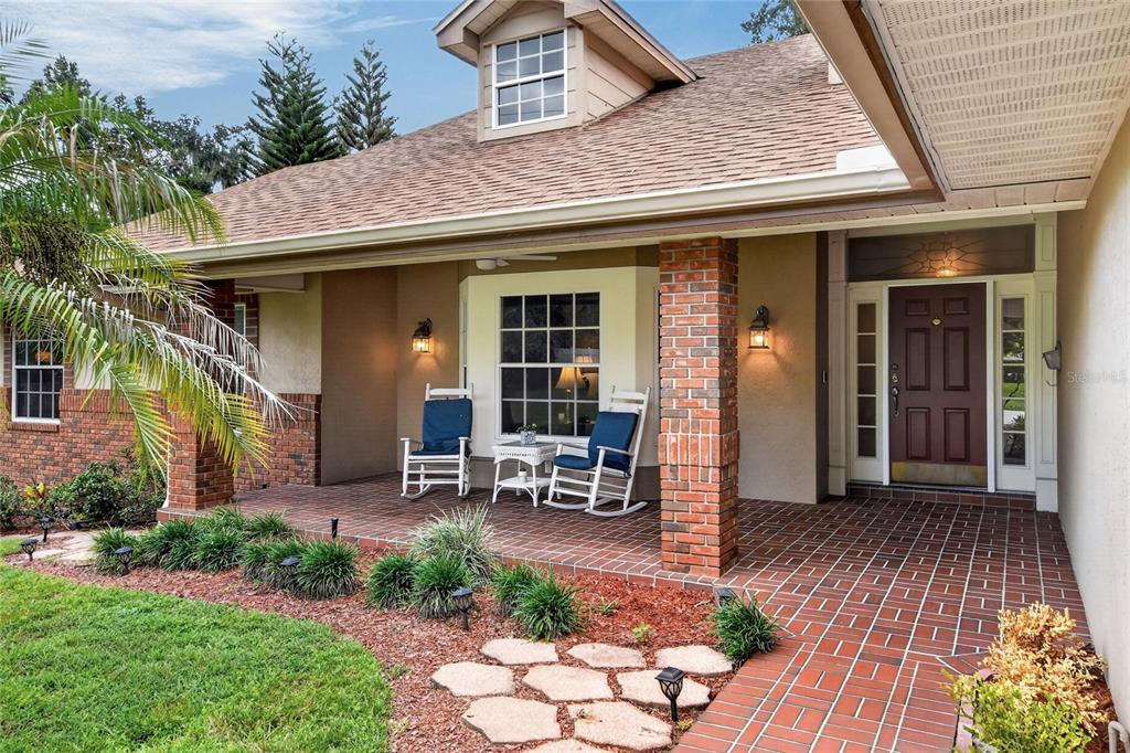 A brick-paved front porch features two rocking chairs, a small table, and a brick pillar — 1221 E EDGEWOOD DRIVE, LAKELAND, FL