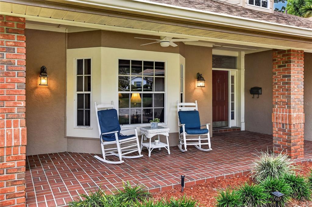 A covered brick porch features two rocking chairs, a small table, and a front door — 1221 E EDGEWOOD DRIVE, LAKELAND, FL
