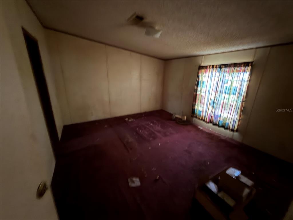 A bedroom with dark red carpeting, paneled walls, and a window with patterned curtains — 45901 MICHIGAN ROAD, ALTOONA, FL