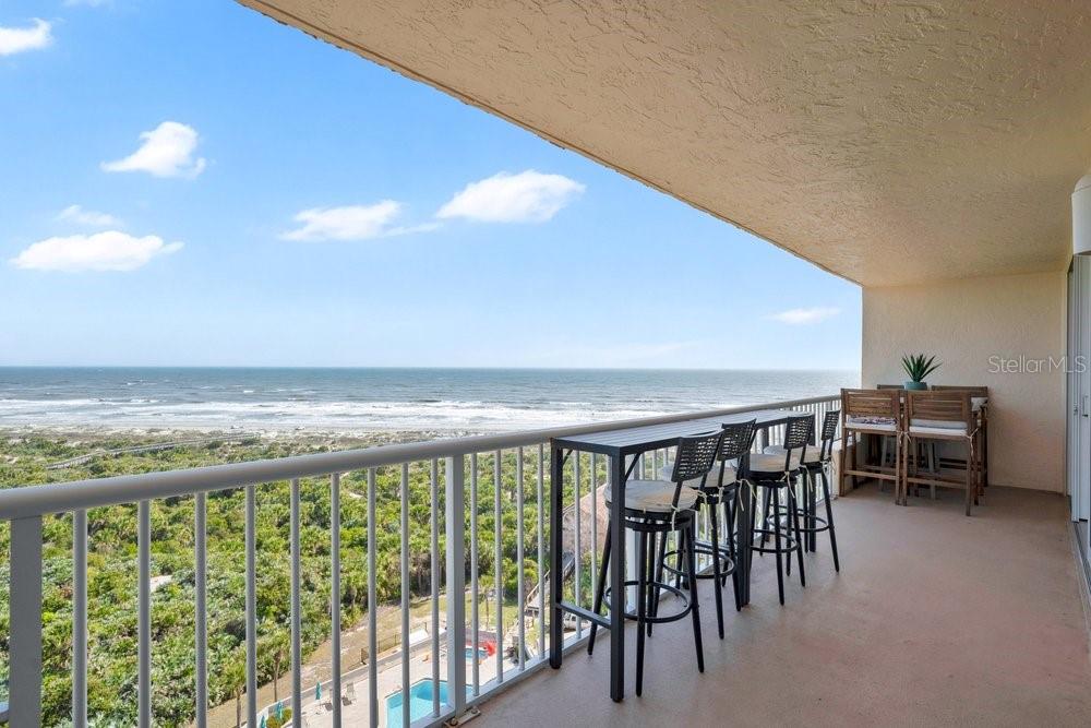 A covered balcony with a white railing overlooks a coastal landscape and nearby buildings — 257 MINORCA BEACH WAY UNIT 1005, NEW SMYRNA BEACH, FL