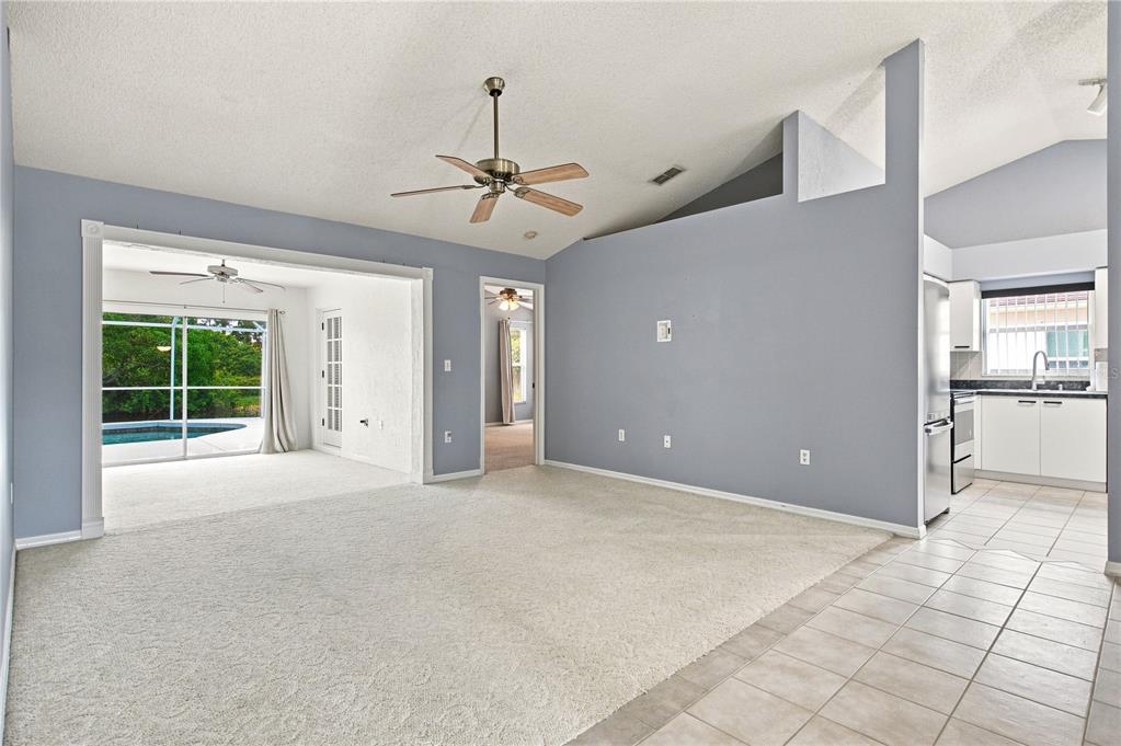 A living room with carpeted floors, a ceiling fan, and an adjacent kitchen and patio — 5311 72ND STREET E, BRADENTON, FL