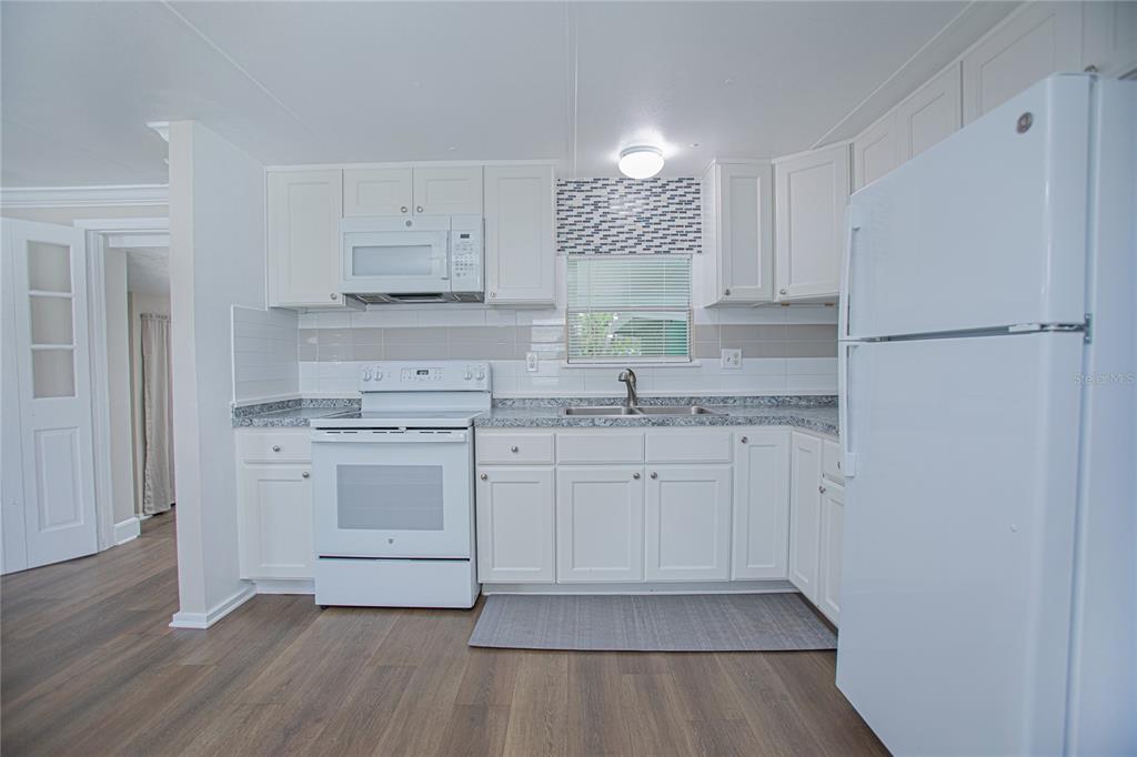A kitchen features white cabinets, a white stove, a microwave, and a white refrigerator — 2009 PINE STREET, ST CLOUD, FL
