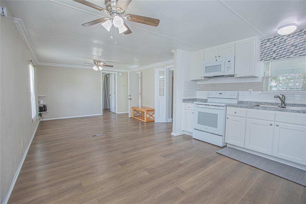 An open-concept kitchen and living area featuring white cabinets, wood-look flooring, and ceiling fans — 2009 PINE STREET, ST CLOUD, FL