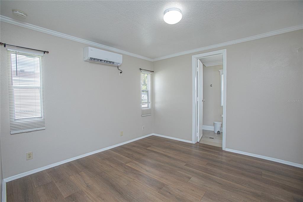A bedroom with light gray walls, wood-look flooring, a wall-mounted AC unit, and an attached bathroom — 2009 PINE STREET, ST CLOUD, FL