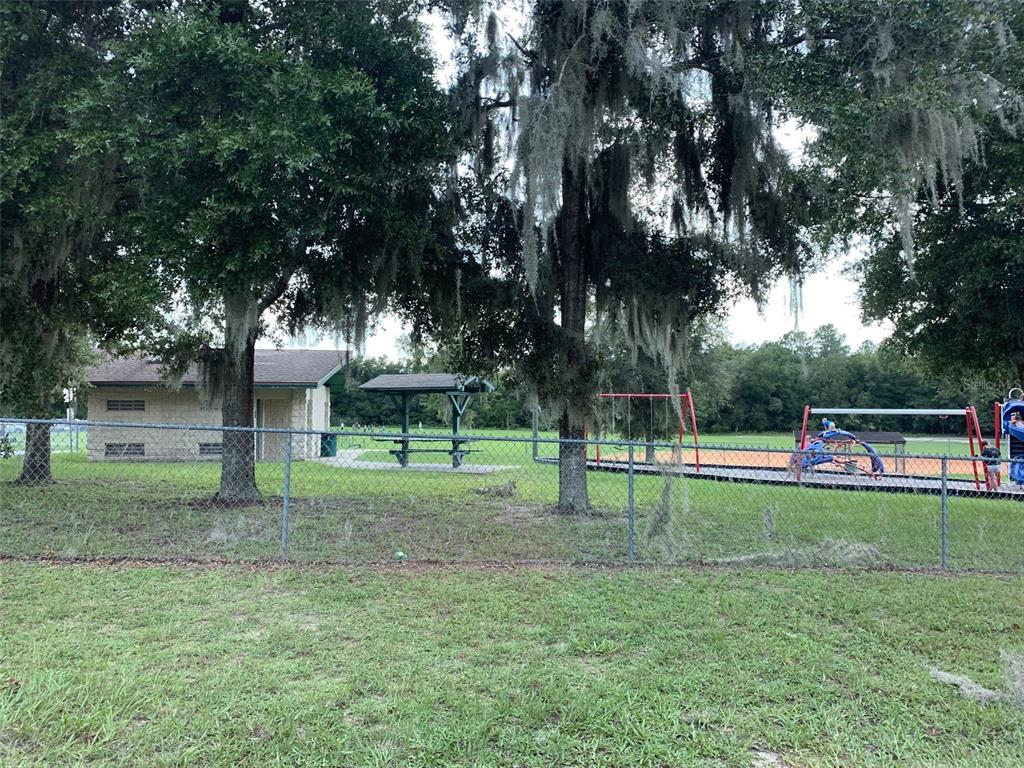 A chain-link fence separates a grassy lawn from a park with a playground and building — 547 W HOMEWAY LOOP, DUNNELLON, FL