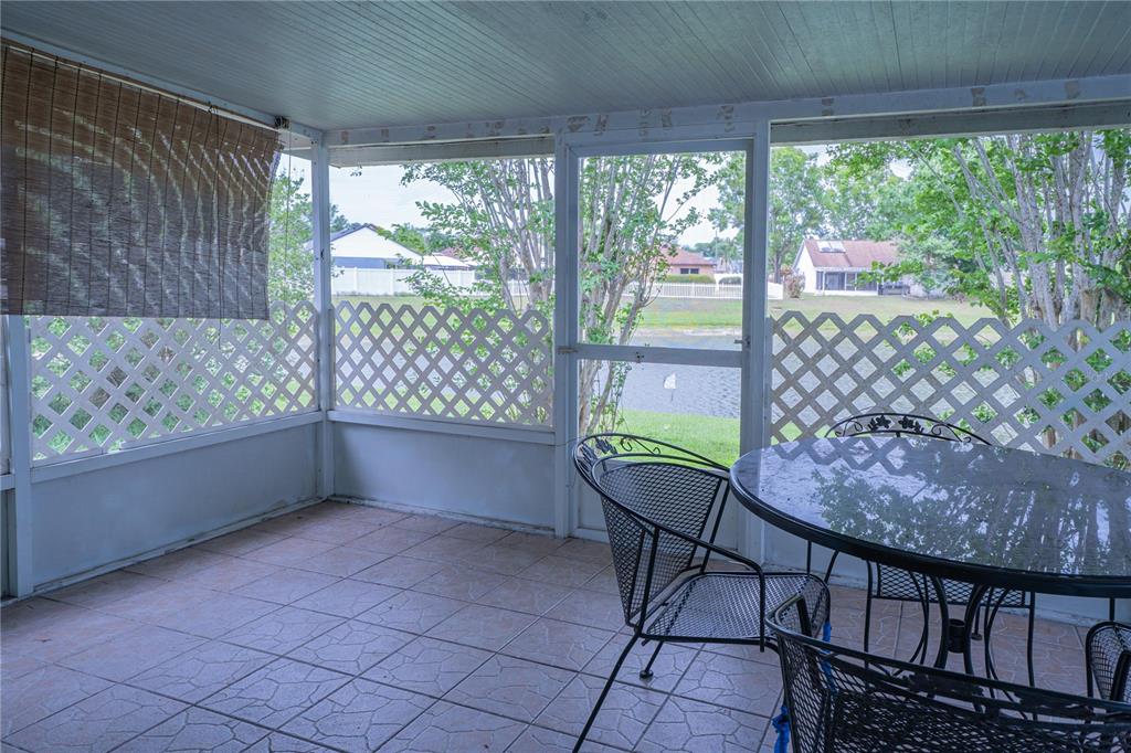A screened-in patio with tile flooring, a glass-top table, and a view of a pond — 6769 EBANS BEND, ORLANDO, FL