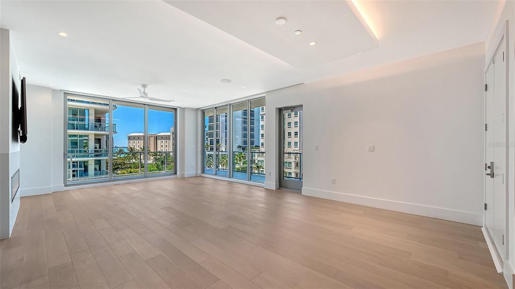 A modern living room with light wood floors, a fireplace, and floor-to-ceiling windows overlooking water — 253 GOLDEN GATE POINT UNIT 401, SARASOTA, FL