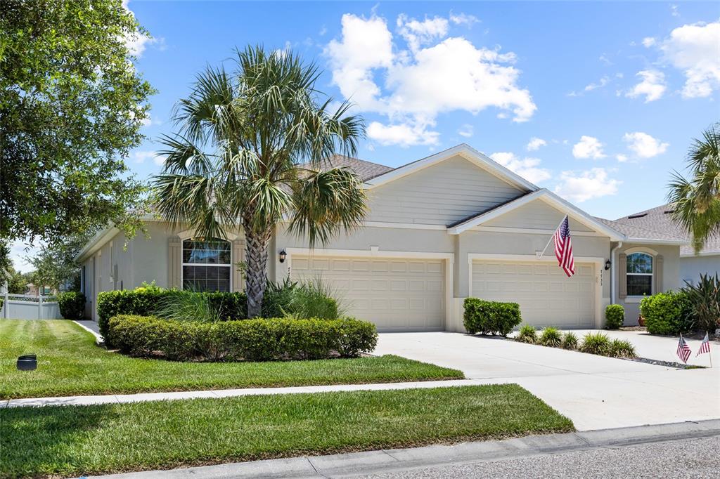 A single-story house with two garage doors, a palm tree, and a manicured lawn — 7727 TIMBERVIEW LOOP, WESLEY CHAPEL, FL