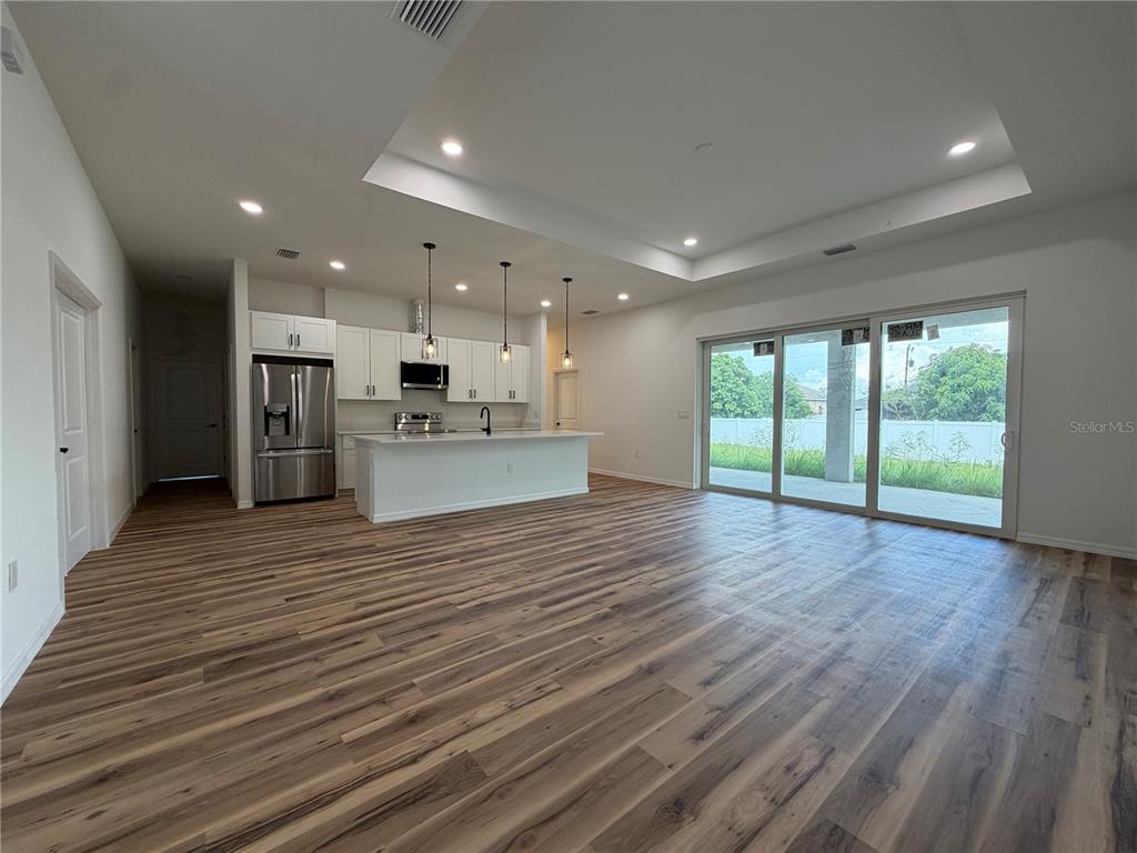 An open-concept kitchen and living area features white cabinetry, a center island, and wood-look flooring — 4210 34TH STREET SW, LEHIGH ACRES, FL