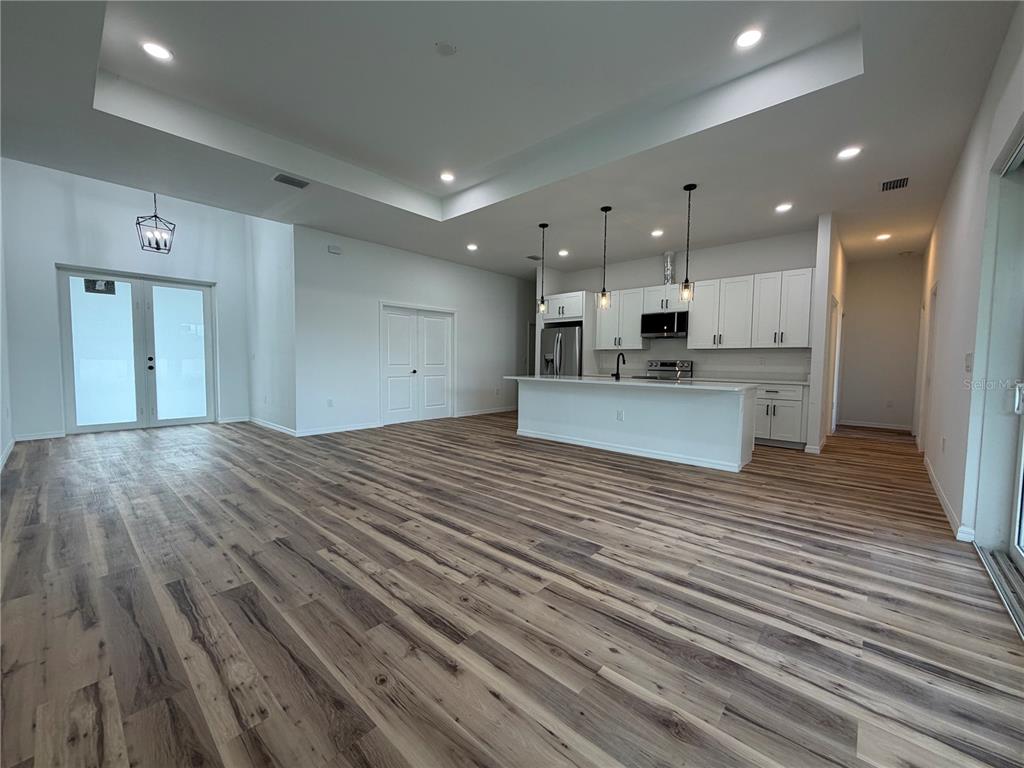 An open-concept kitchen and living area features white cabinetry, a central island, and wood-look flooring — 4210 34TH STREET SW, LEHIGH ACRES, FL
