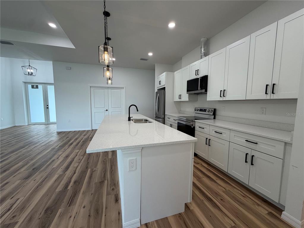A modern kitchen features white cabinetry, a quartz-topped island, and wood-look flooring — 4210 34TH STREET SW, LEHIGH ACRES, FL