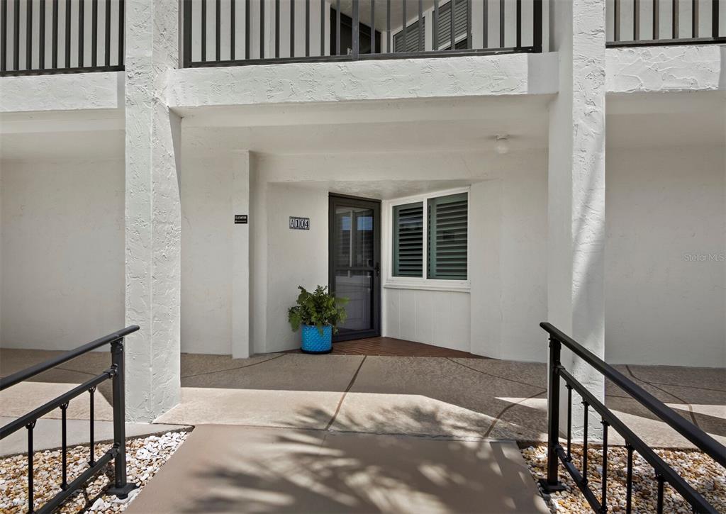 The exterior entrance of a ground-floor unit features a glass door, a potted plant, and railings — 448 GULF OF MEXICO DRIVE UNIT A104, LONGBOAT KEY, FL