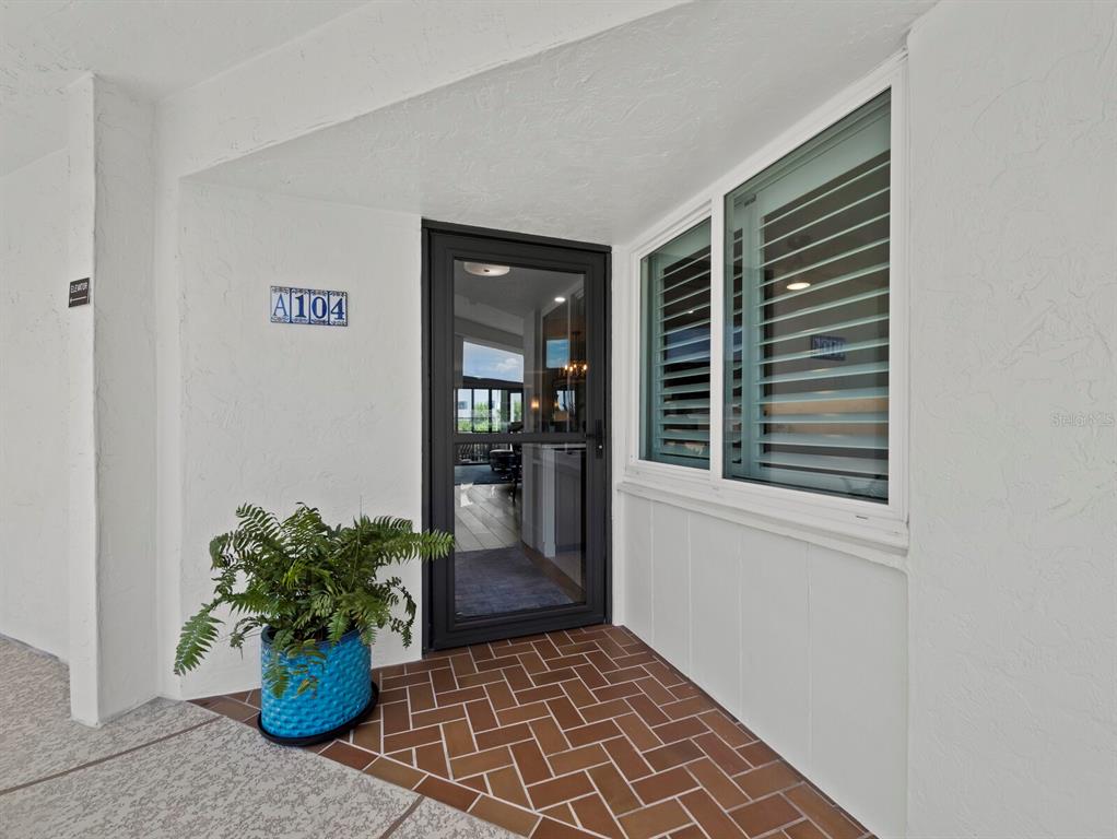 The entrance to unit A104 features a glass storm door, a potted fern, and brick flooring — 448 GULF OF MEXICO DRIVE UNIT A104, LONGBOAT KEY, FL