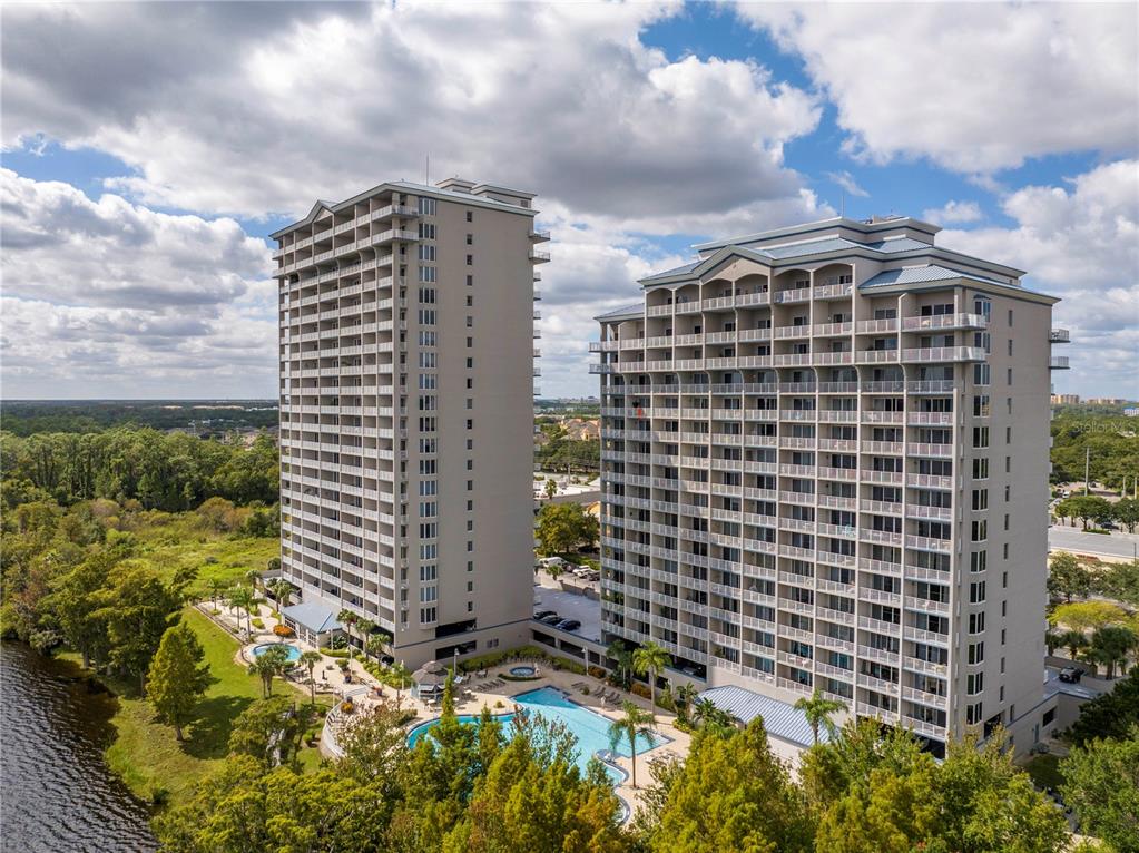 An aerial view shows two tall, light-colored residential towers situated beside a large lake — 13415 BLUE HERON BEACH DRIVE UNIT 109, ORLANDO, FL
