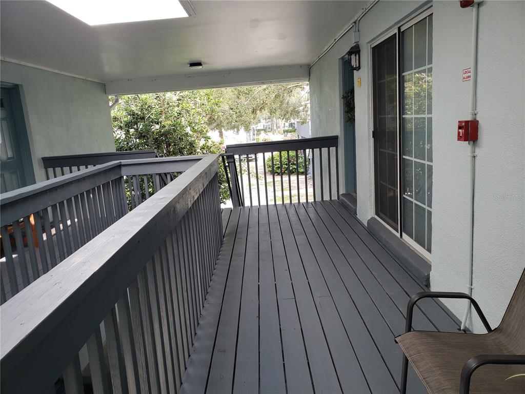 A covered outdoor balcony features gray wooden decking, a matching railing, and a sliding glass door — 4886 CONWAY ROAD UNIT 76, ORLANDO, FL