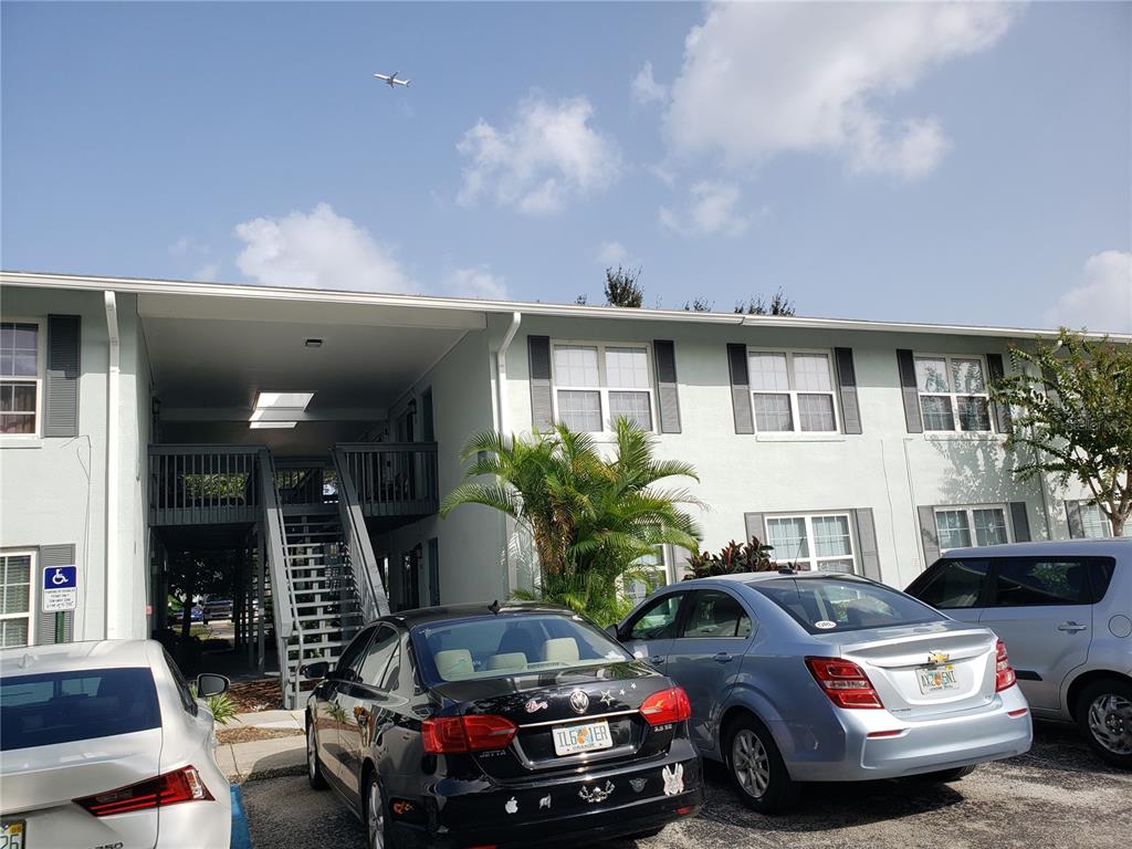 A multi-story apartment building exterior features a central staircase and a parking lot with cars — 4886 CONWAY ROAD UNIT 76, ORLANDO, FL