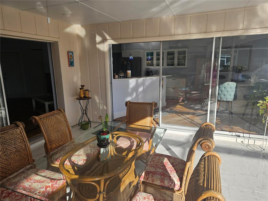 A sunroom features a glass-topped rattan dining set and sliding doors looking into a kitchen — 43 WINDSOR DRIVE, ENGLEWOOD, FL