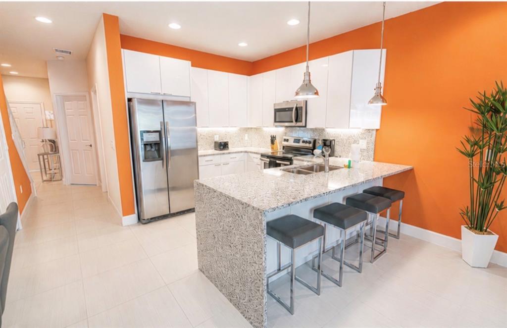 A modern kitchen features white cabinets, granite countertops, stainless steel appliances, and bright orange walls — 1603 TRANQUIL AVENUE, CLERMONT, FL