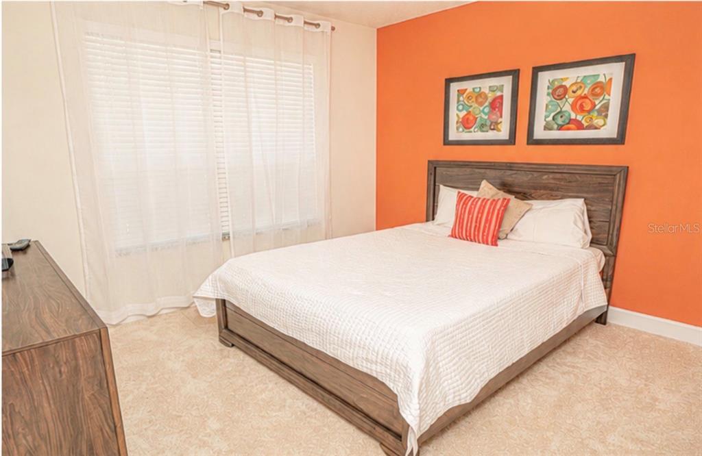 A bedroom features a bed with a wooden frame against an orange accent wall — 1603 TRANQUIL AVENUE, CLERMONT, FL
